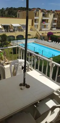 a table with an umbrella on a balcony with a pool at Appartement T2 avec piscine, proche de la plage et du Port in Gruissan