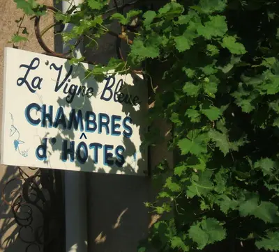 a sign on a pole next to a bush with a sign at La Vigne Bleue in Olonzac