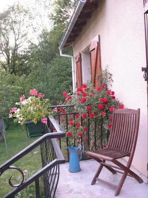 a chair sitting on a porch with red flowers at Le Moulin du Barthas in Montredon-Labessonnié