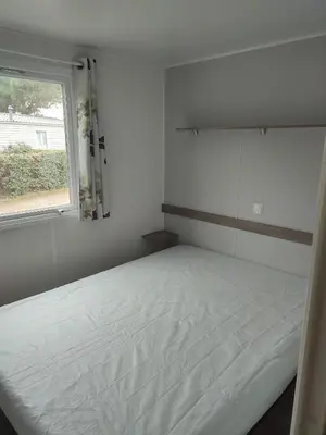 a white bedroom with a bed and a window at Mobil home in Port-la-Nouvelle