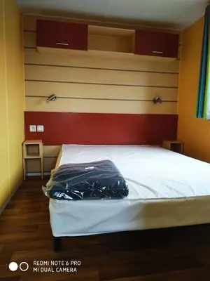 a bedroom with a bed with white sheets and wood floors at Mobil home au bord du lac in Nages