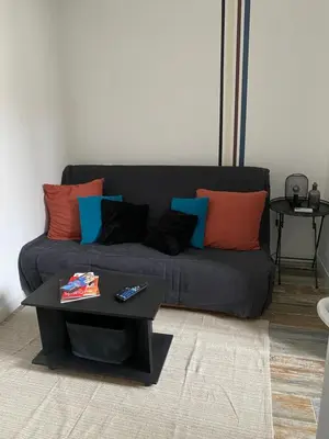 a black couch with colorful pillows and a coffee table at Au pied du centre ville - Mignon petit studio climatisé in Narbonne
