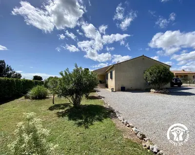 a building with a tree next to a gravel driveway at Les iris in Castelnau-dʼAude