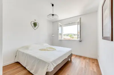 a white bedroom with a bed in a room with a window at La Villa d'Isa et Seb in Narbonne