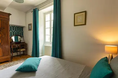a bedroom with a bed with blue curtains and a window at Domaine La Belle Histoire - Gîte côté Parc in Besset