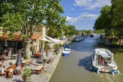a boat is docked in a canal with people sitting at tables at Maison de village 8 couchages in La Livinière