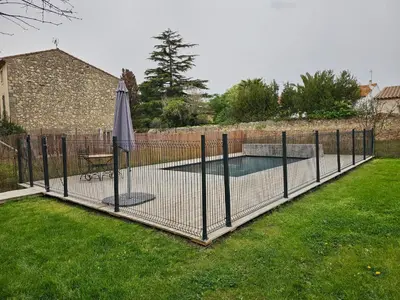 a fence with a tennis court and an umbrella at Grande Maison Vigneronne, proche de la mer in Salles-d'Aude