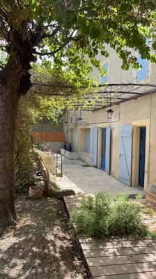 a building with blue doors and a tree next to it at Grande Maison Vigneronne, proche de la mer in Salles-d'Aude
