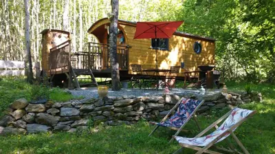 a log cabin with a table and a red umbrella at Terra bosca roulotte in Cambounès