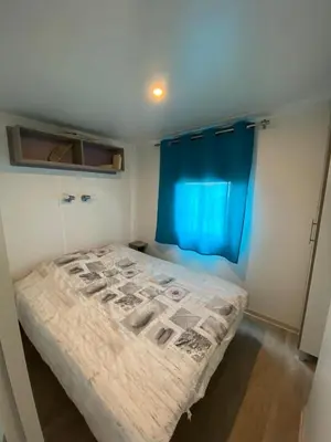 a small bedroom with a bed with a blue curtain at MH148 camping NOVELA - location entre particuliers-Mobil home 6pl climatisé - in Port-la-Nouvelle