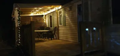 a patio with a table and chairs on a deck at night at MH148 camping NOVELA - location entre particuliers-Mobil home 6pl climatisé - in Port-la-Nouvelle