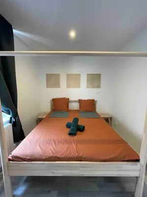a bed with an orange blanket and a black object on it at Vivez Castelnaudary à pied, T2 cosy avec jardin, proche gare et canal du midi in Castelnaudary