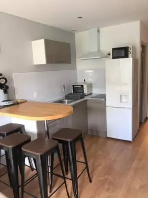 a kitchen with a wooden table and chairs and a refrigerator at Appartement rénové RDC terrasse 200m plage in Port-la-Nouvelle