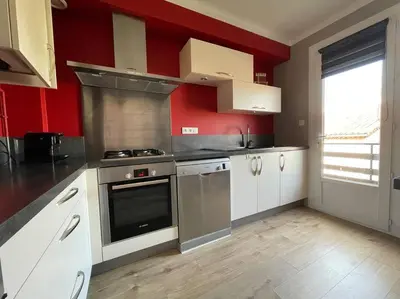 a kitchen with white cabinets and a red wall at Appartement 2 chambres +parking in Narbonne