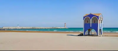 a blue shack on the beach with a pier in the background at Le studio du Port in Port-la-Nouvelle