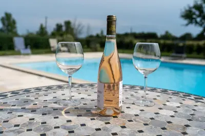 two wine glasses and a bottle on a table next to a pool at Chez PhiL in La Pomarède