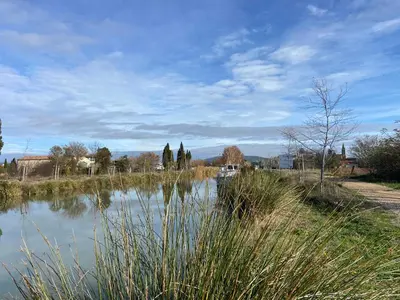 a body of water with trees and buildings in the background at T3 bord canal du midi, piscine in Homps