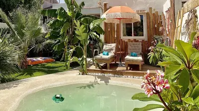 a swimming pool in a garden with two chairs and an umbrella at Tropical Lodge SPA Narbonne in Narbonne
