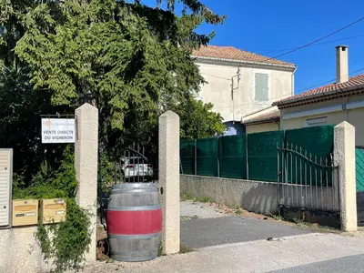 a fence with a barrel in front of a house at Du côté de chez nous in Cuxac-dʼAude