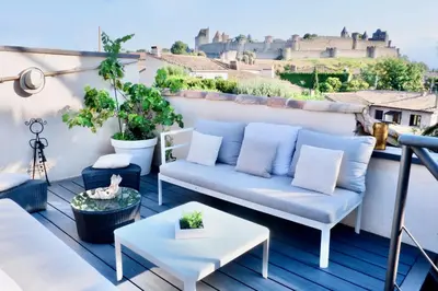 a patio with a couch and a table on a balcony at La Maison Blanche 5*, Piscine & vue Cité Médiévale in Carcassonne