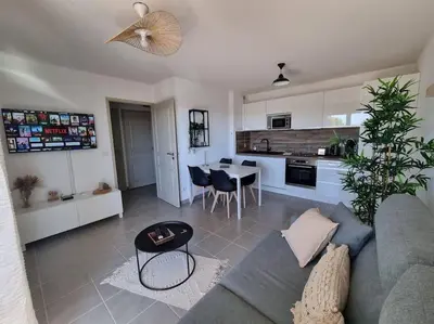 a living room with a couch and a table and a kitchen at L'Appartement Ensoleillé, WIFI-Clim-Gare-Terrasse in Narbonne