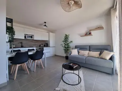 a living room with a couch and a kitchen at L'Appartement Ensoleillé, WIFI-Clim-Gare-Terrasse in Narbonne