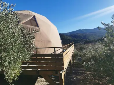 a yurt with a wooden deck and mountains in the background at Le dôme géodésique in Ansignan
