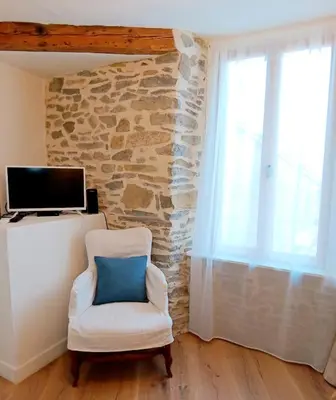 a white chair with a blue pillow in a room with a stone wall at La Petite Romance - Gîte 3 étoiles in Siran