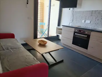 a living room with a table and a couch and a kitchen at Le Rubis in Gruissan