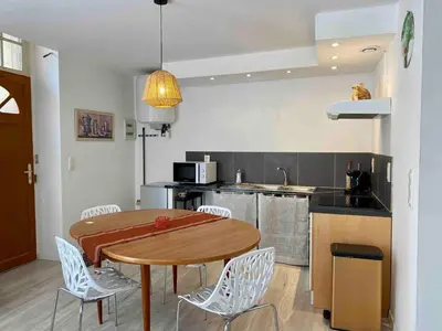 a kitchen with a wooden table and white chairs at Accueillant petit T2 cœur de centre ville in Lézignan-Corbières