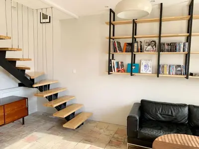 a living room with a black leather couch and wooden stairs at La Grande Traverse gîte d'exception de bord de mer in Lapalme