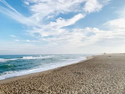 a beach with people walking on the sand and the ocean at La Grande Traverse gîte d'exception de bord de mer in Lapalme