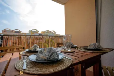 a wooden table with plates and glasses on a balcony at Logis des Goélands YourHostHelper in Gruissan