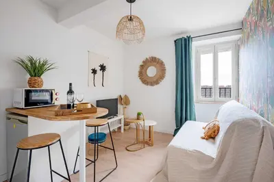 a room with a bed and a kitchen with a table at Le Tropical : T2 rénové Ambiance Cosy et Colorée in Mazamet