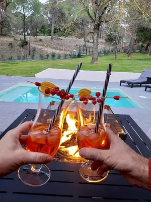 a person holding two wine glasses in front of a fire at Le Clos FMR - Romain in Malves-en-Minervois