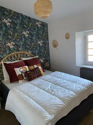 a bedroom with a large white bed with floral wallpaper at Cosy T3 dans corps de ferme l écureuil in Vieillevigne