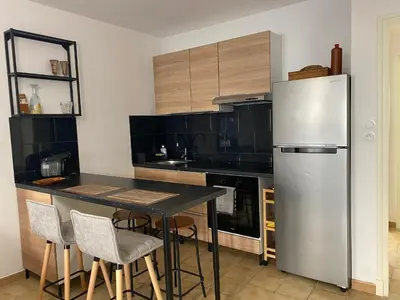 a kitchen with a stainless steel refrigerator and a table at Confortable T2 avec jardin aménagé in Lézignan-Corbières