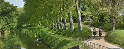 two people riding bikes down a path next to a river at Vue sur Cité - SPA in Carcassonne