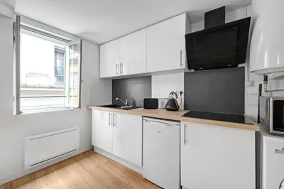 a white kitchen with white cabinets and a window at Les studios Jean Bringer - Carcassonne centre-ville in Carcassonne