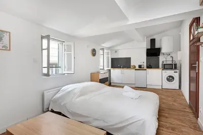 a white bedroom with a bed and a kitchen at Les studios Jean Bringer - Carcassonne centre-ville in Carcassonne