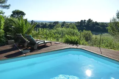 a swimming pool with two chairs on a wooden deck at Chalet, quiet, with view and pool (at summertime) in Ventenac-Cabardès