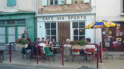 a group of people sitting at tables outside a cafe des sports at Gite rue Tranquille in Padern