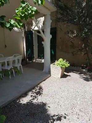 a patio with a tree and white chairs and a building at Sigean - Maison domaine viticole, 6 km de la mer in Sigean