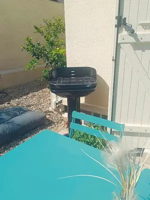 a grill and a blue chair next to a building at Studio Oasis Narbonne Terrasse & Calme in Narbonne