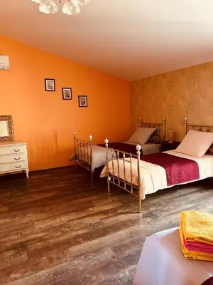 two beds in a bedroom with orange walls and wooden floors at La Babayaga in Capestang