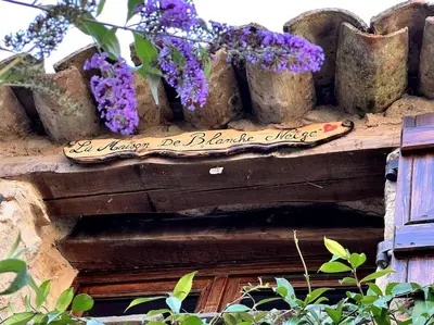 a sign on the side of a building with purple flowers at La Maison De Blanche Neige in Assignan