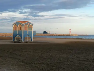 a small building on the beach with a lighthouse in the background at Entre Mer et Roseaux - Piscine chauffée - Proche centre et mer - Animaux bienvenus in Port-la-Nouvelle