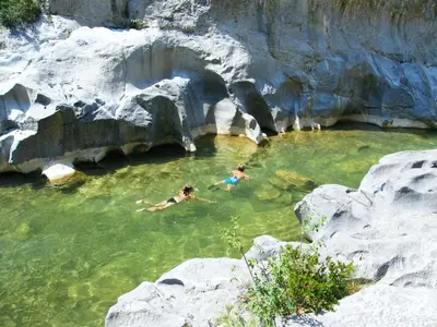 two people swimming in a pool of water next to rocks at Gîte Les Mimosas in Prugnanes