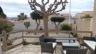 a patio with a table and chairs and a tree at Appartement spacieux de plein pied avec 2 chambres, cuisine, salon, terrasse à 2 minutes de la plage in Gruissan