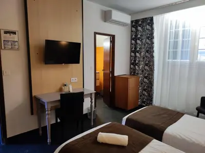 a hotel room with two beds and a desk and a television at Hôtel et Appart'Hôtel Le Relais Du Val D'Orbieu in Ornaisons